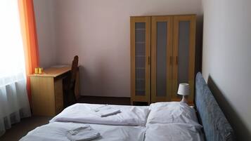A bedroom with a bed, a desk, a wardrobe, and a lamp.