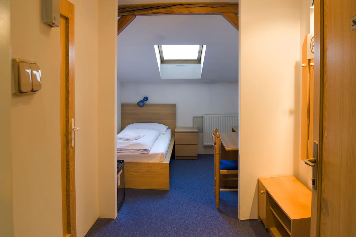 A narrow hallway leading to a bedroom with a skylight, a bed, a bedside table, and a chair.