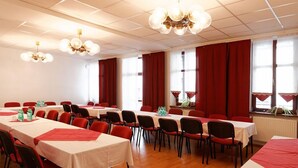 Un salón de conferencias con varias mesas, sillas rojas y candelabros.