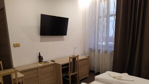 Una habitación de hotel con escritorio, dos camas, televisor y ventana con cortinas.