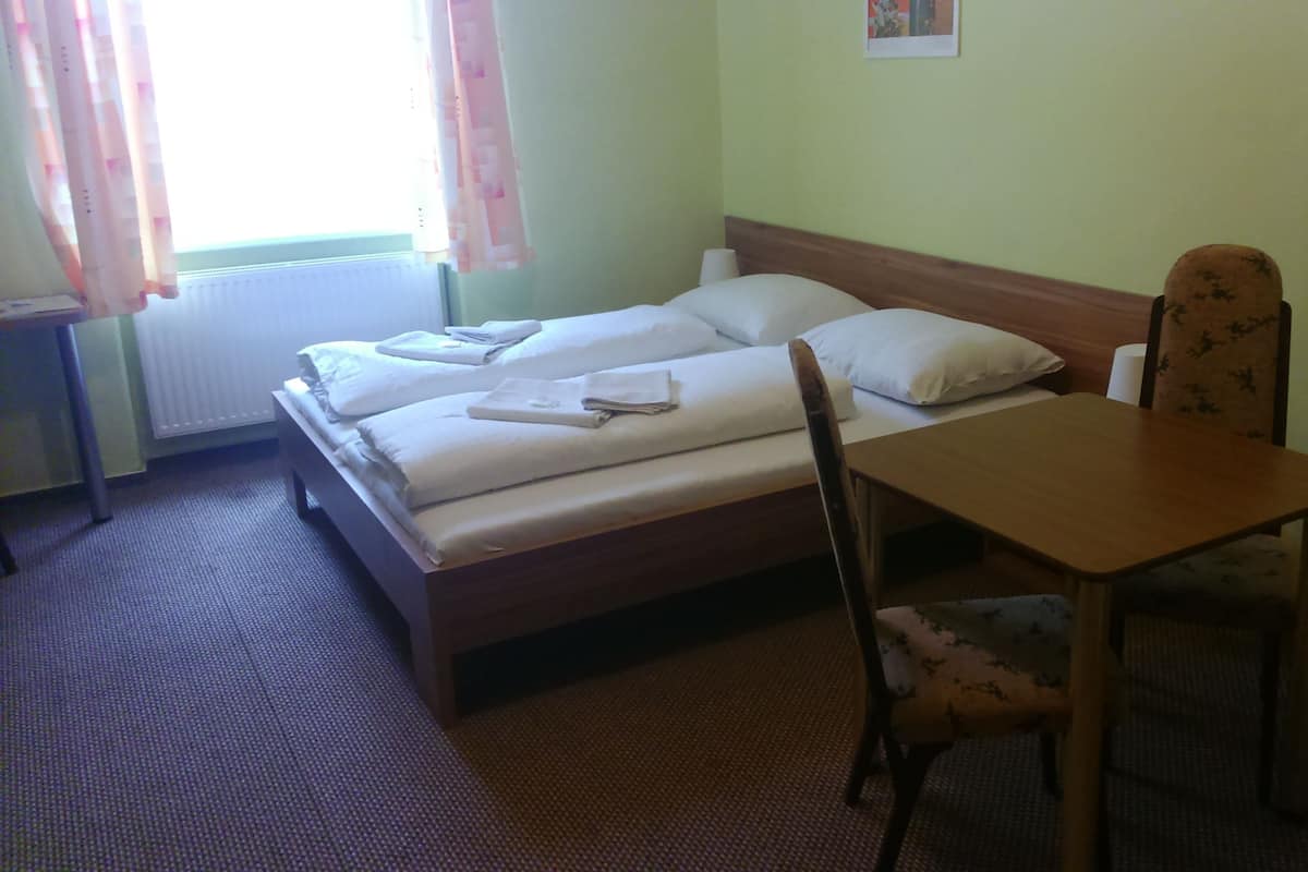 A simple hotel room with a bed, a wooden table, and a chair.