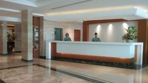 Zona de recepción de un hotel con suelo de mármol, mostrador de recepción y dos empleados.