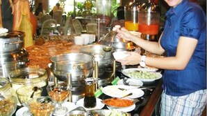 Mesa de buffet con diversos alimentos y una persona sirviendo.
