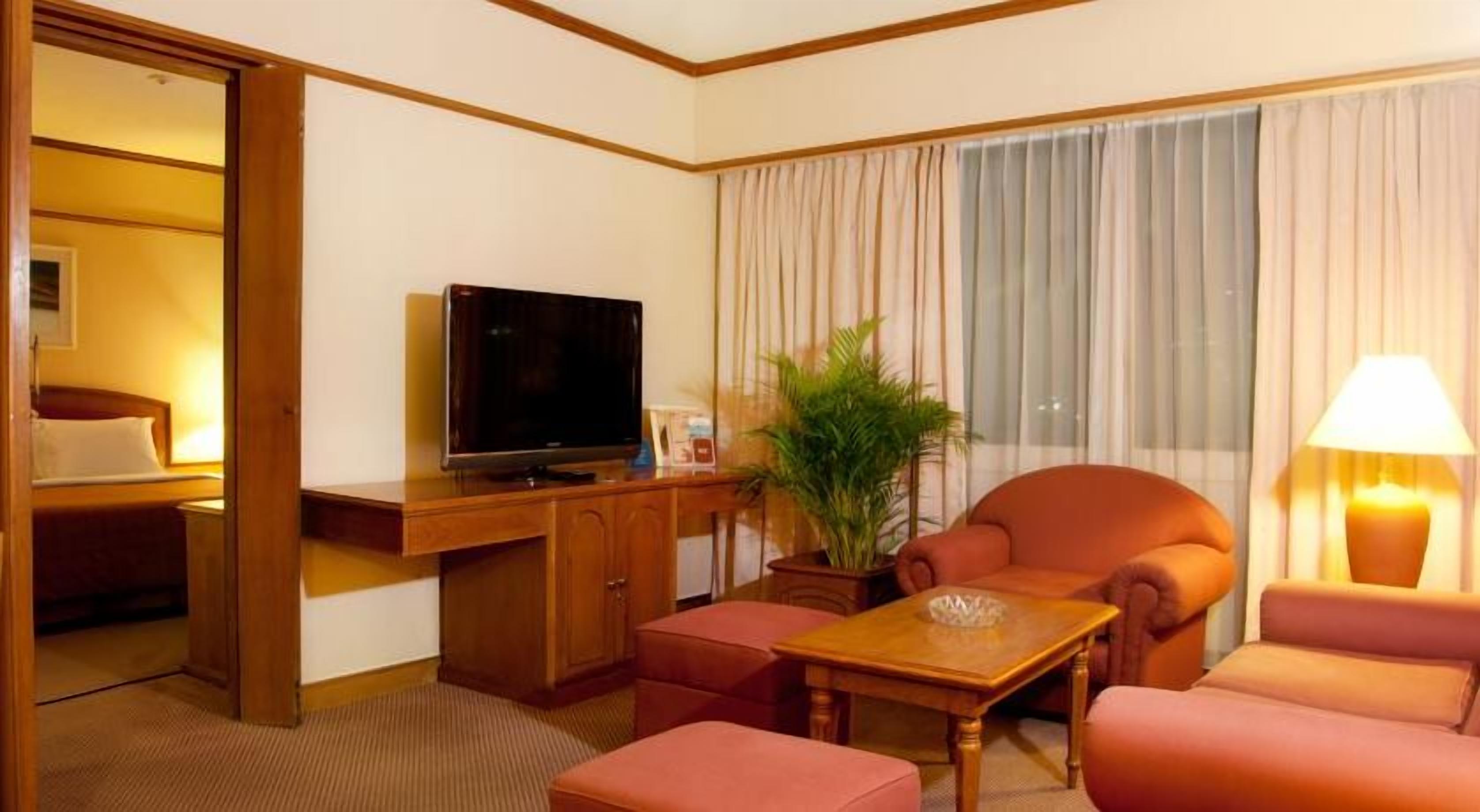 A hotel room with a wooden desk, a television, a potted plant, and a sofa.