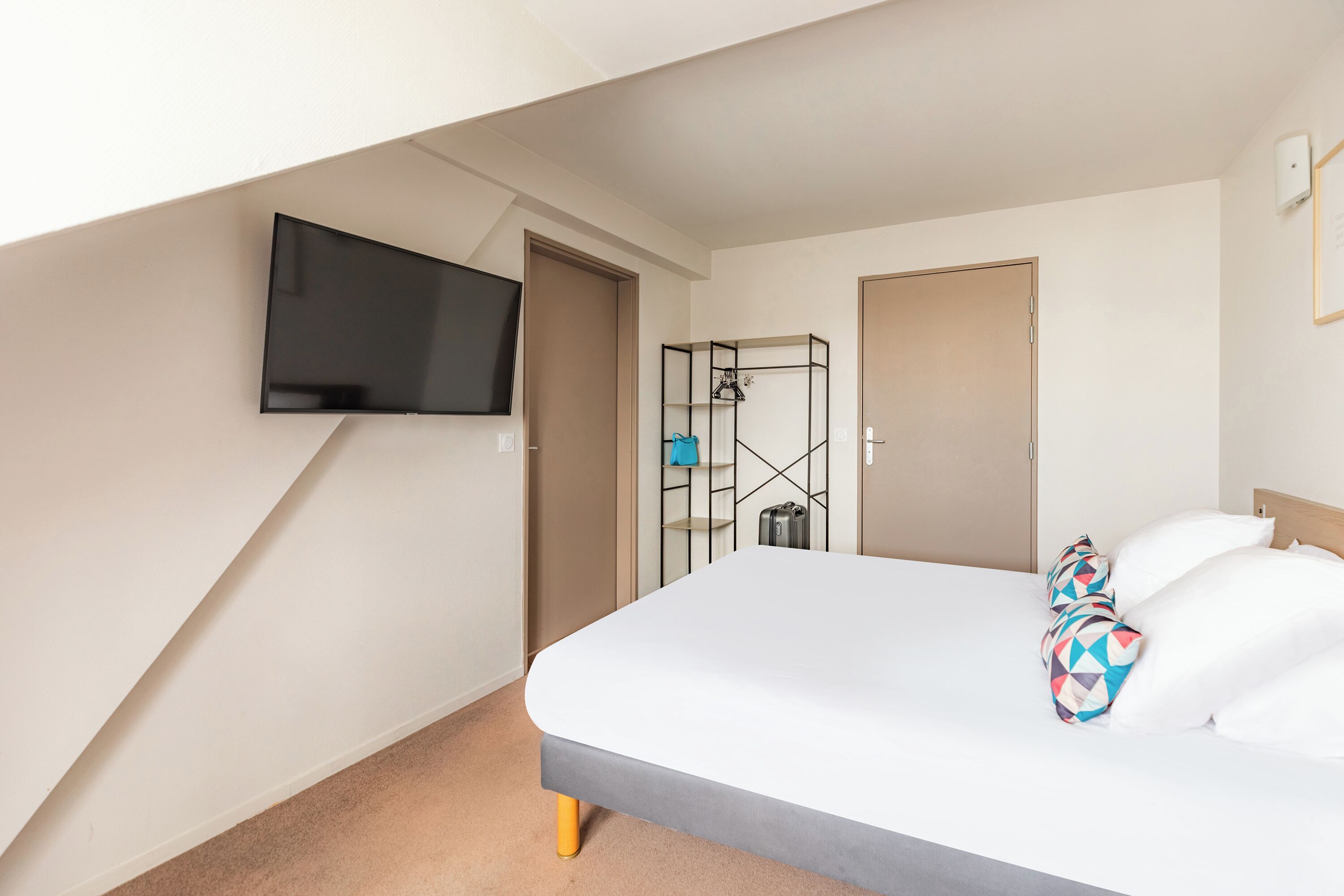 Une chambre d’hôtel avec un lit, un téléviseur fixé au mur et une armoire.