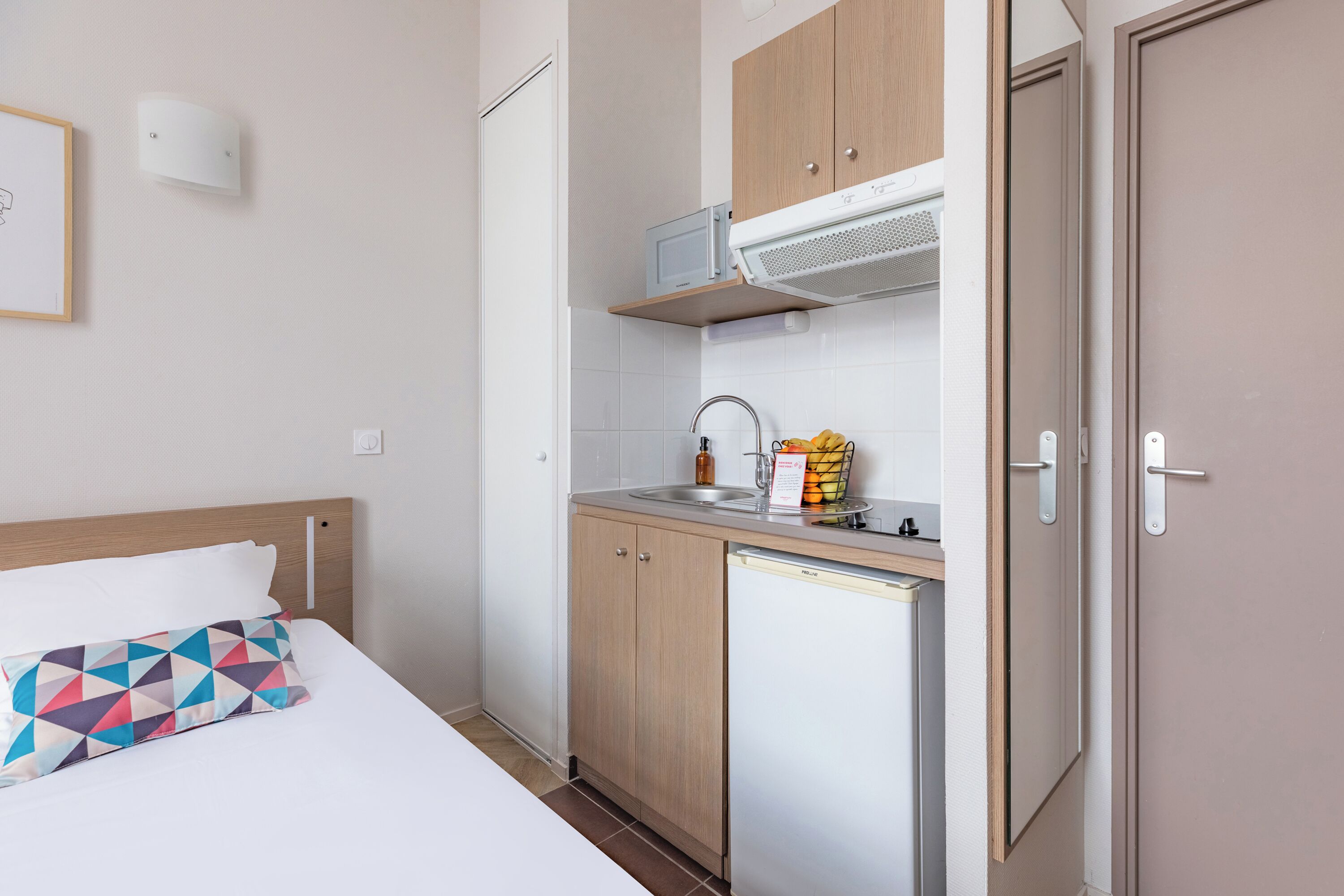 Ein kleines Hotelzimmer mit Bett, einer kompakten Küchenzeile, einer Mikrowelle und einem Waschbecken.