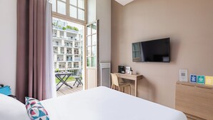 A hotel room with a bed, a desk, a TV, and a balcony with a view of other buildings. - Appart'City Confort Reims Centre (Reims)