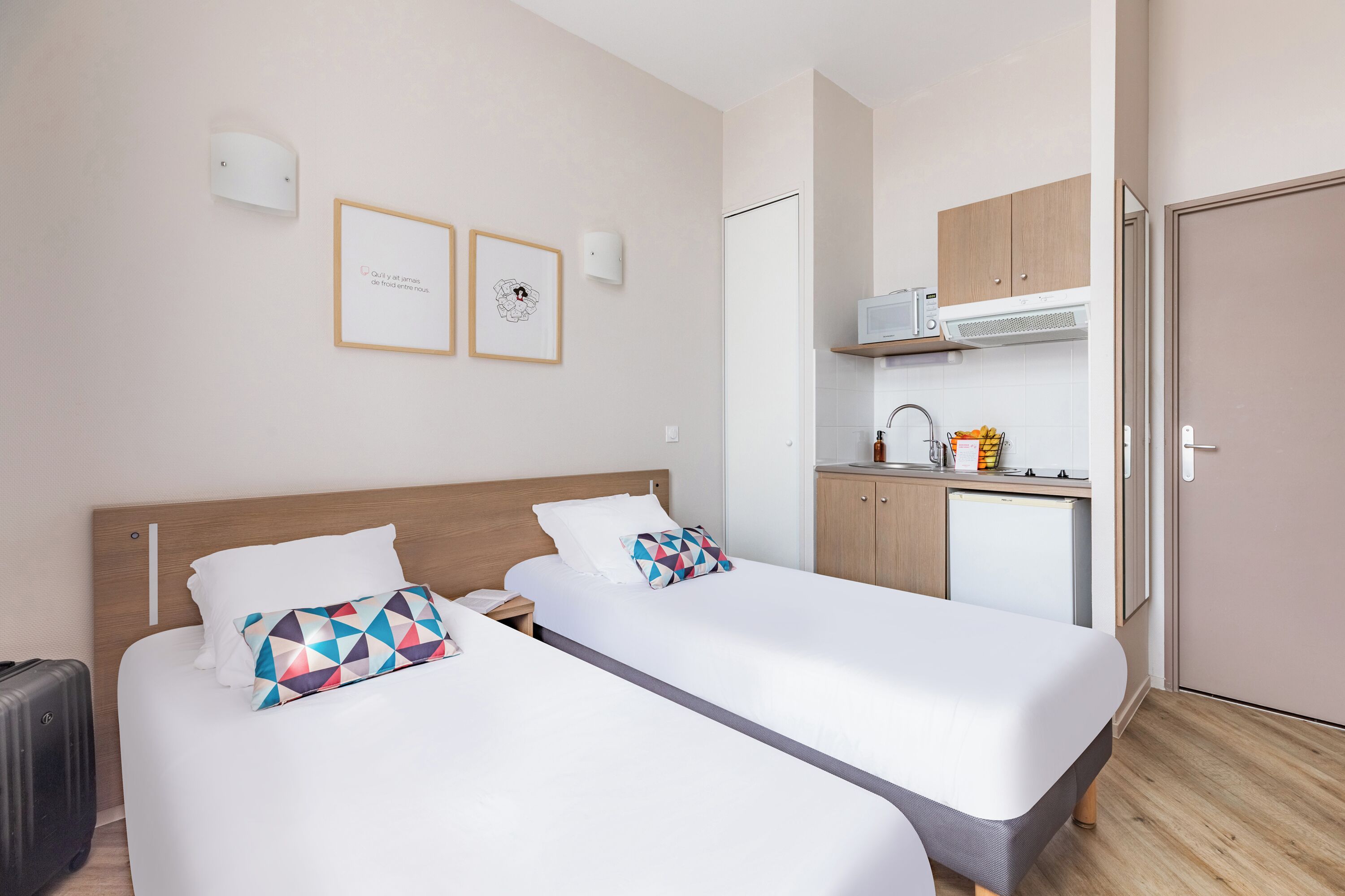 Une chambre d’hôtel avec deux lits, une kitchenette et une porte donnant sur la salle de bain.
