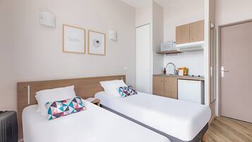 Une chambre d’hôtel avec deux lits, une kitchenette et une porte donnant sur la salle de bain.