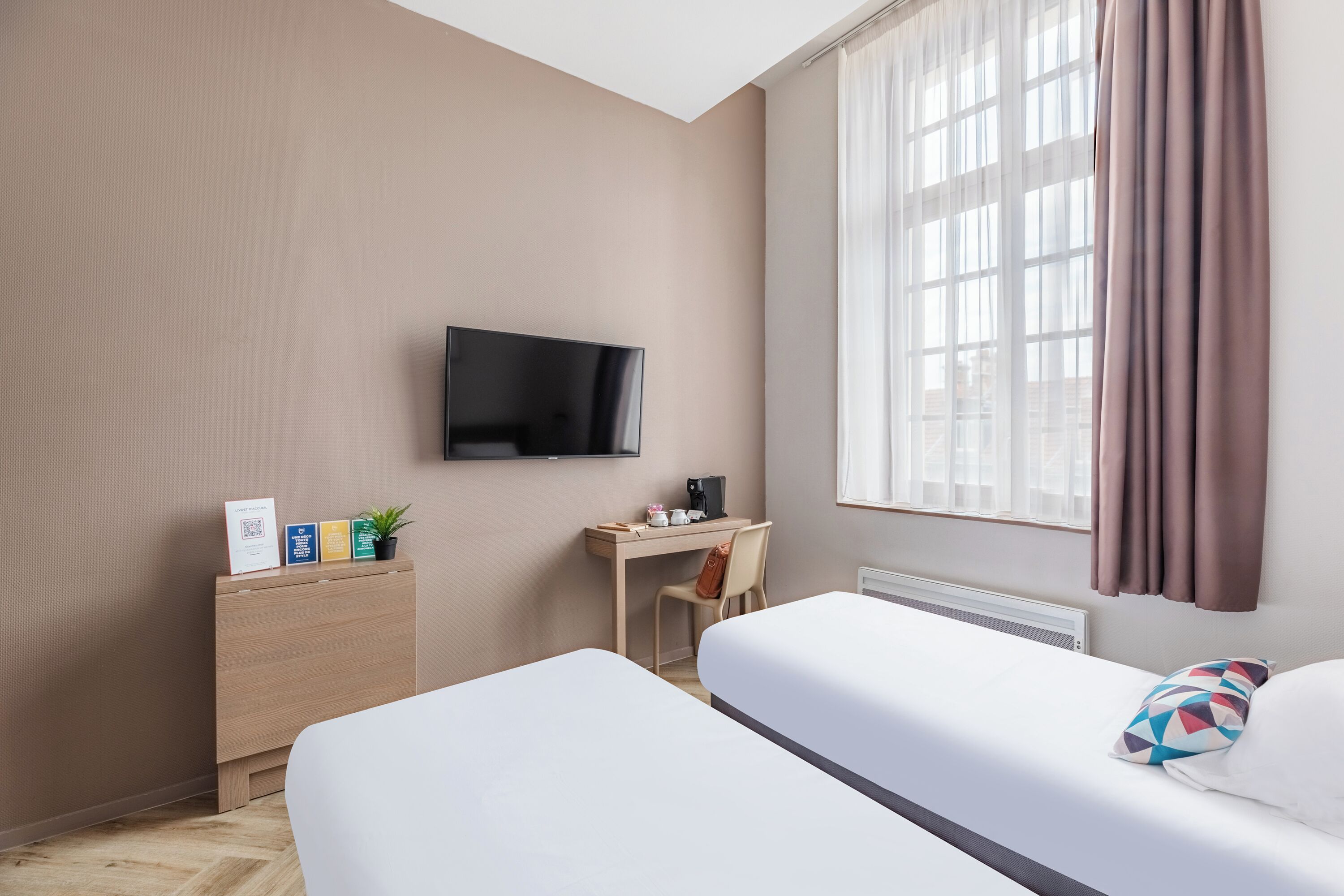 A hotel room with two beds, a desk, a chair, a TV, and a window with curtains.