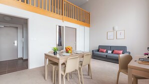A modern living room with a dining area, a grey sofa, and a wooden staircase. - Appart'City Confort Reims Centre (Reims)
