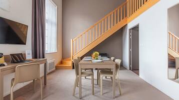 A modern living space with a dining area, a TV mounted on the wall, and a staircase.
