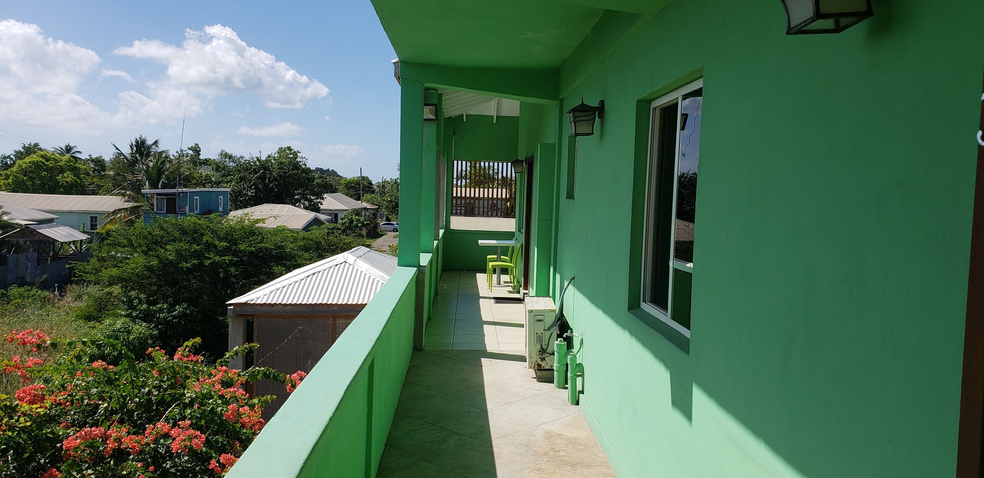 Un edificio verde con un balcón estrecho, una mesa pequeña y una silla.