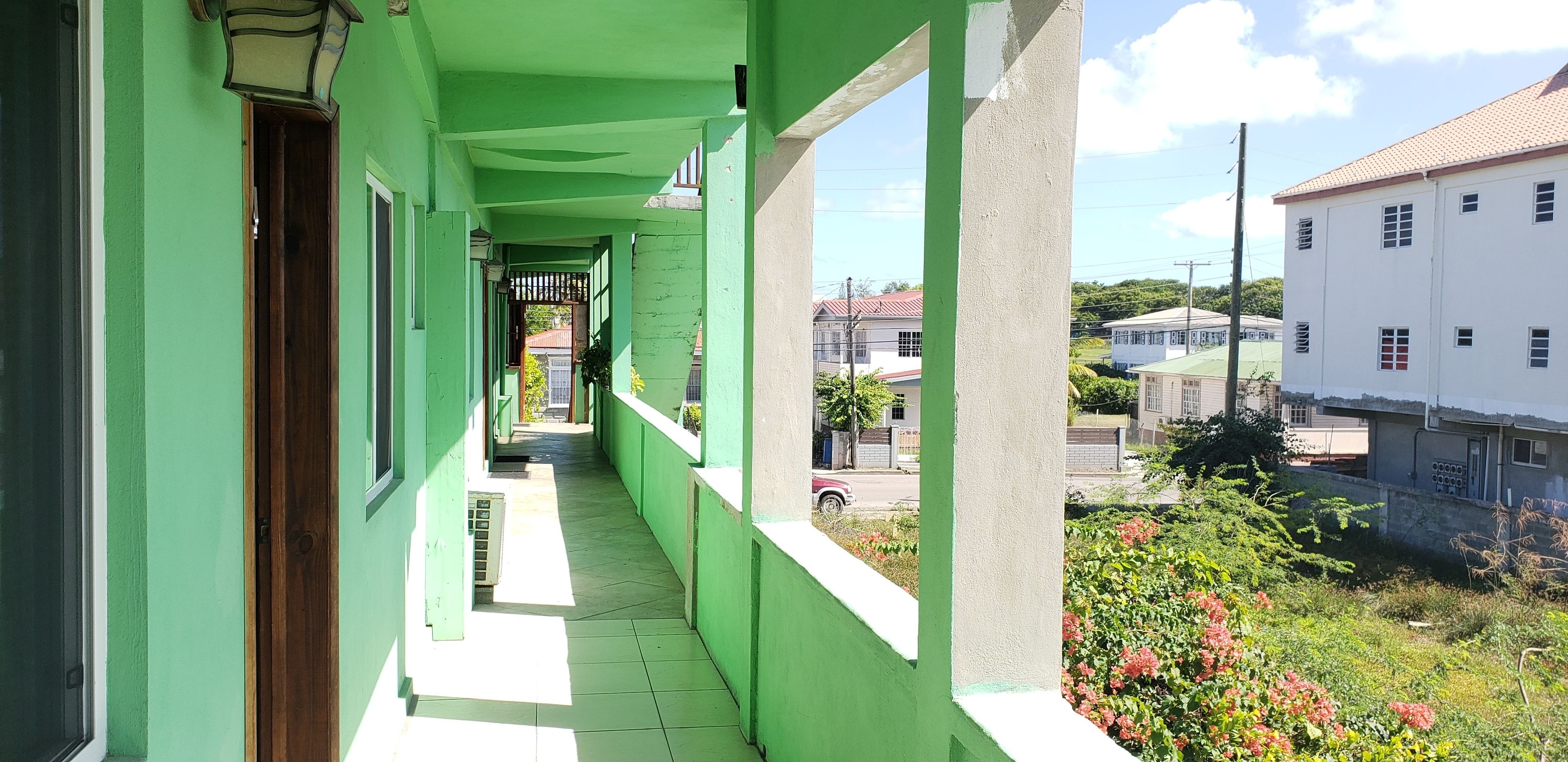 A narrow corridor with green walls and a white railing, leading to a gate.