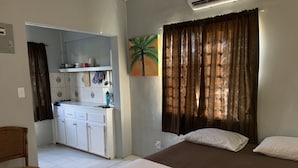 Una habitación de hotel con cama, una silla, kitchenette y un cuadro de una palmera.