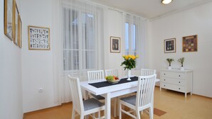 A dining area with a white table, chairs, and a vase with flowers. There are framed pictures on the walls and a white cabinet with plants. - Mivos Prague Apartments Vltava (Prague)
