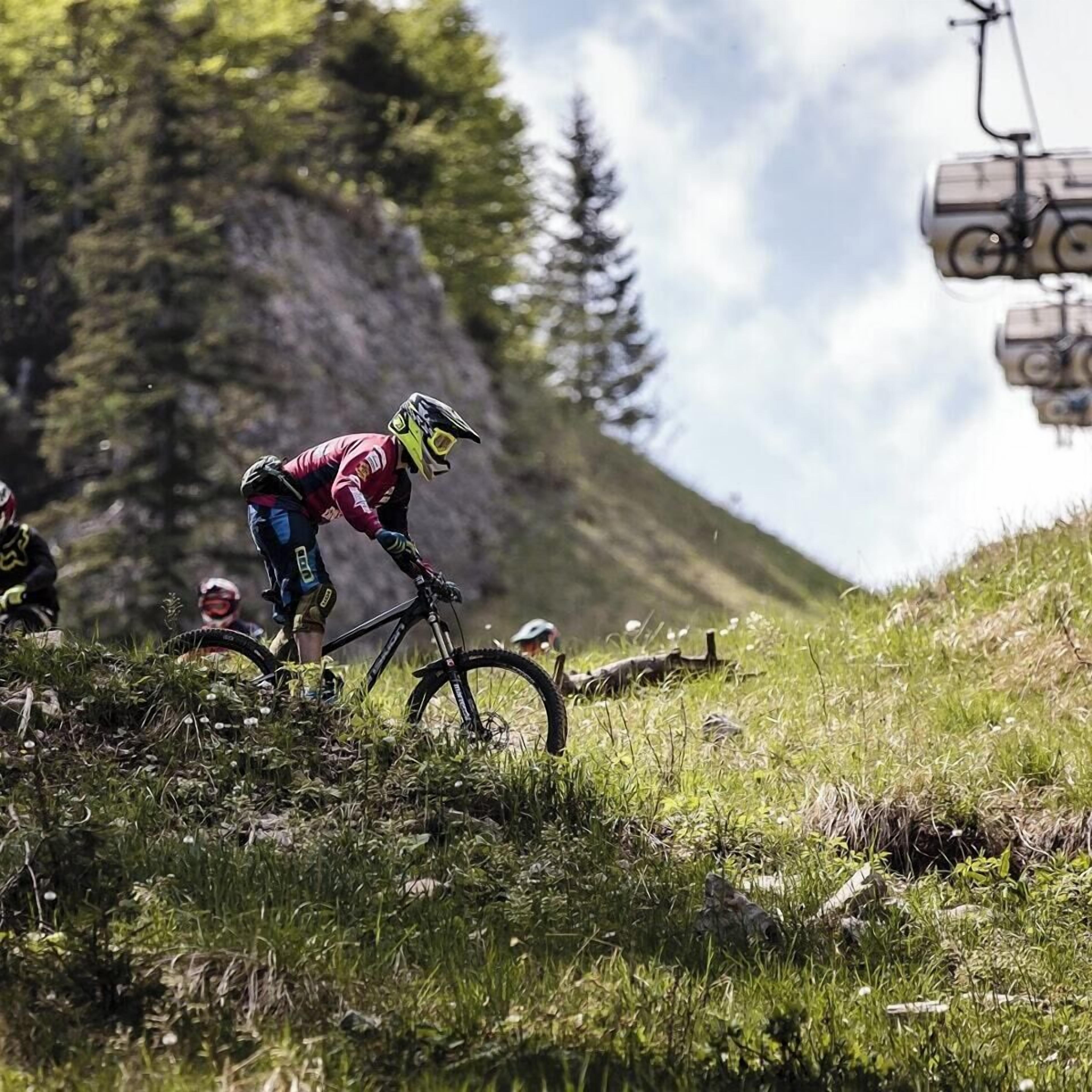 Een mountainbiker op een pad, met een stoeltjeslift op de achtergrond.