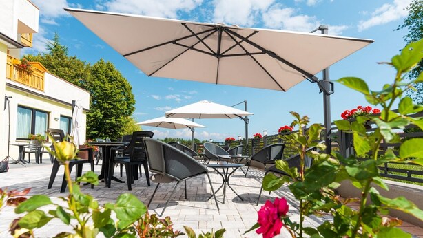 An outdoor patio with tables and chairs, large umbrellas, and a view of a building and trees. - Hotel Fai (Fai della Paganella)