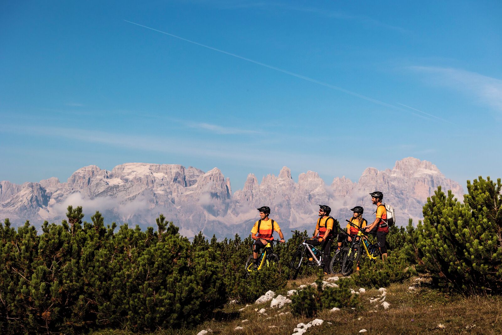 Un grupo de ciclistas de montaña pedaleando por un sendero con montañas al fondo.