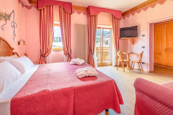A hotel room with a bed, two chairs, a TV, and a view of the outside. - Hotel Fai (Fai della Paganella)