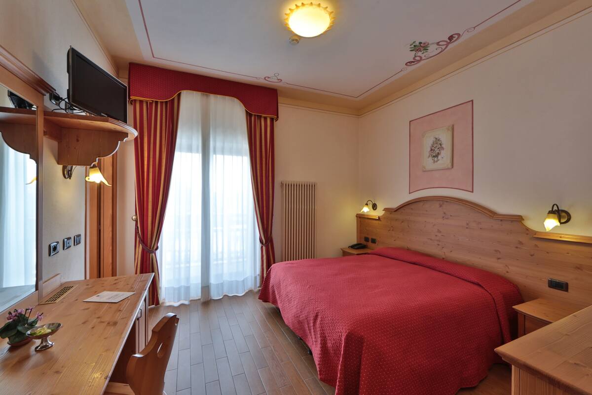 A hotel room with a wooden bed, a wooden desk, a television on a stand, a radiator, and a picture on the wall.