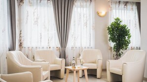 A room with four beige leather armchairs arranged around a small wooden table with a bottle and glass. - Hotel Fai (Fai della Paganella)