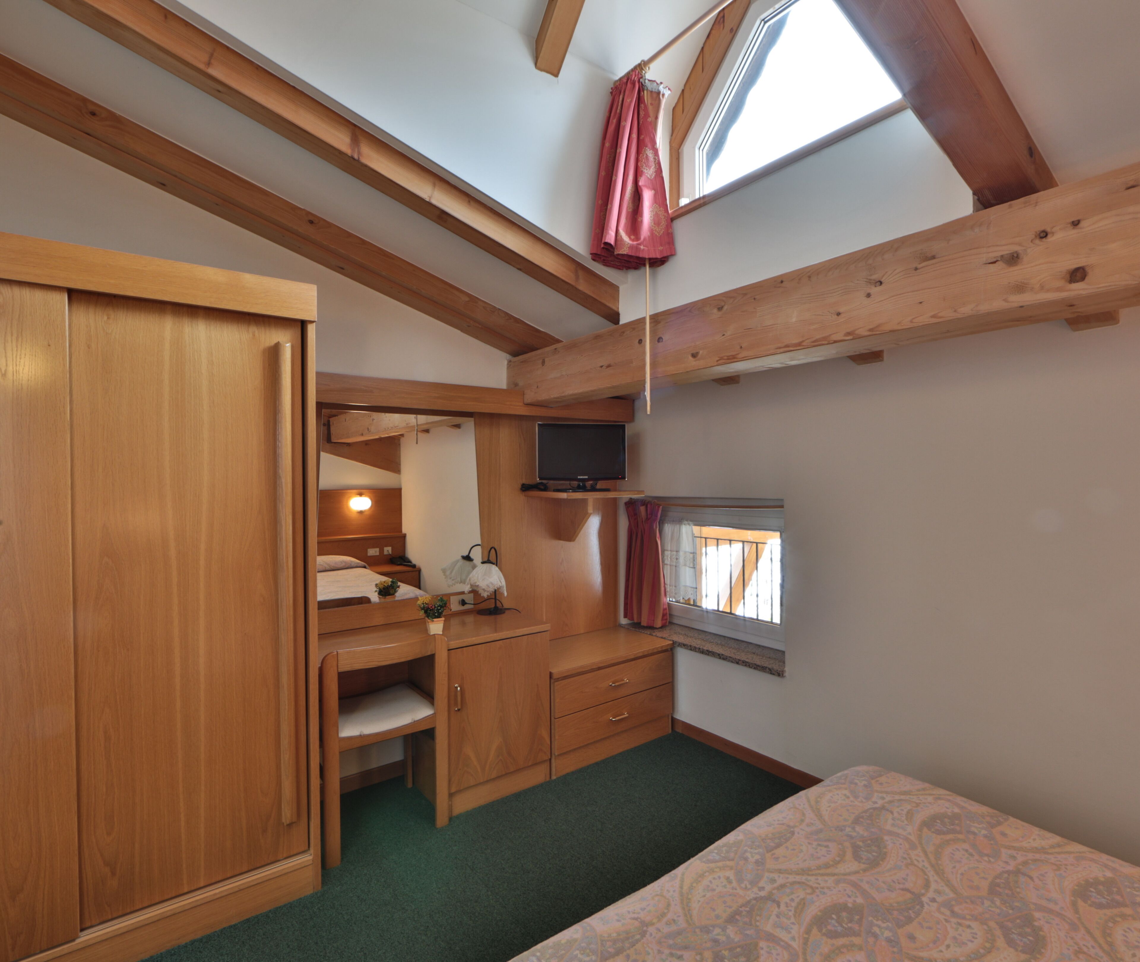 A compact bedroom with a bunk bed, a desk with a chair, a television, and a window with curtains.