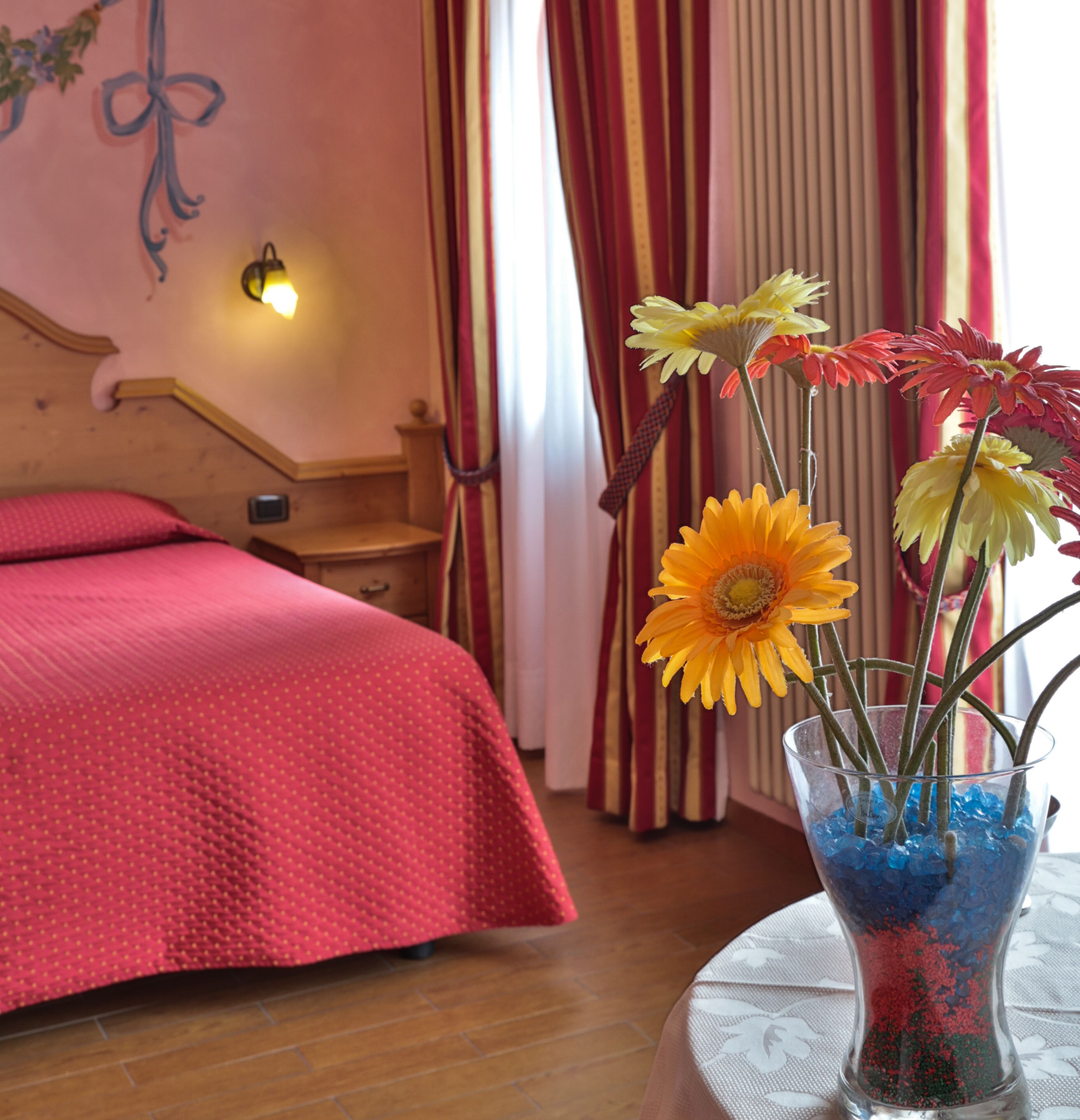A bedroom with a wooden headboard, a red bedspread, and a vase with flowers on a table.