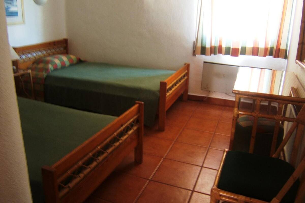 A small, cozy room with two wooden beds, a wooden chair, and a window with curtains.