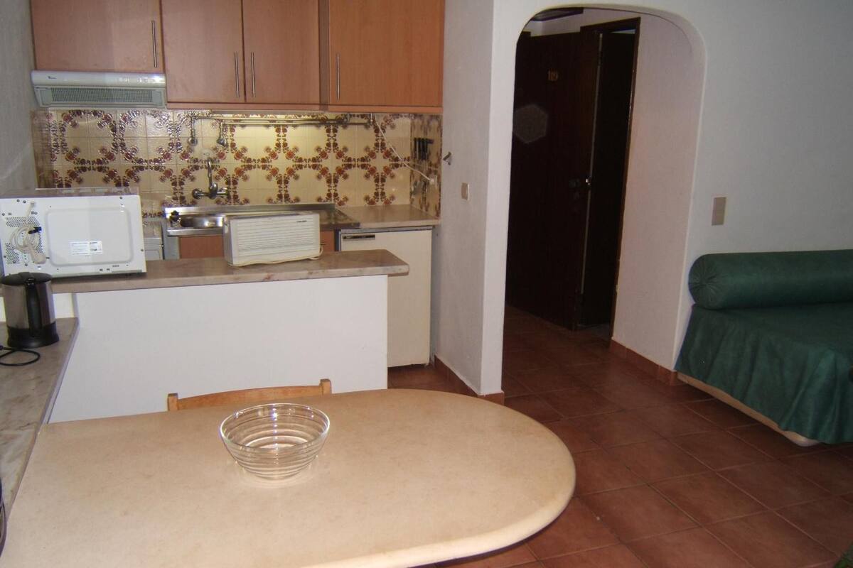 A compact kitchen with a dining table, a microwave, a radio, and a green sofa in the adjacent living area.