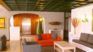 A modern living room with a sofa, armchairs, and a coffee table. There is a fireplace with a decorative piece above it. - Solar de São João - Apartamentos Turísticos (Albufeira)