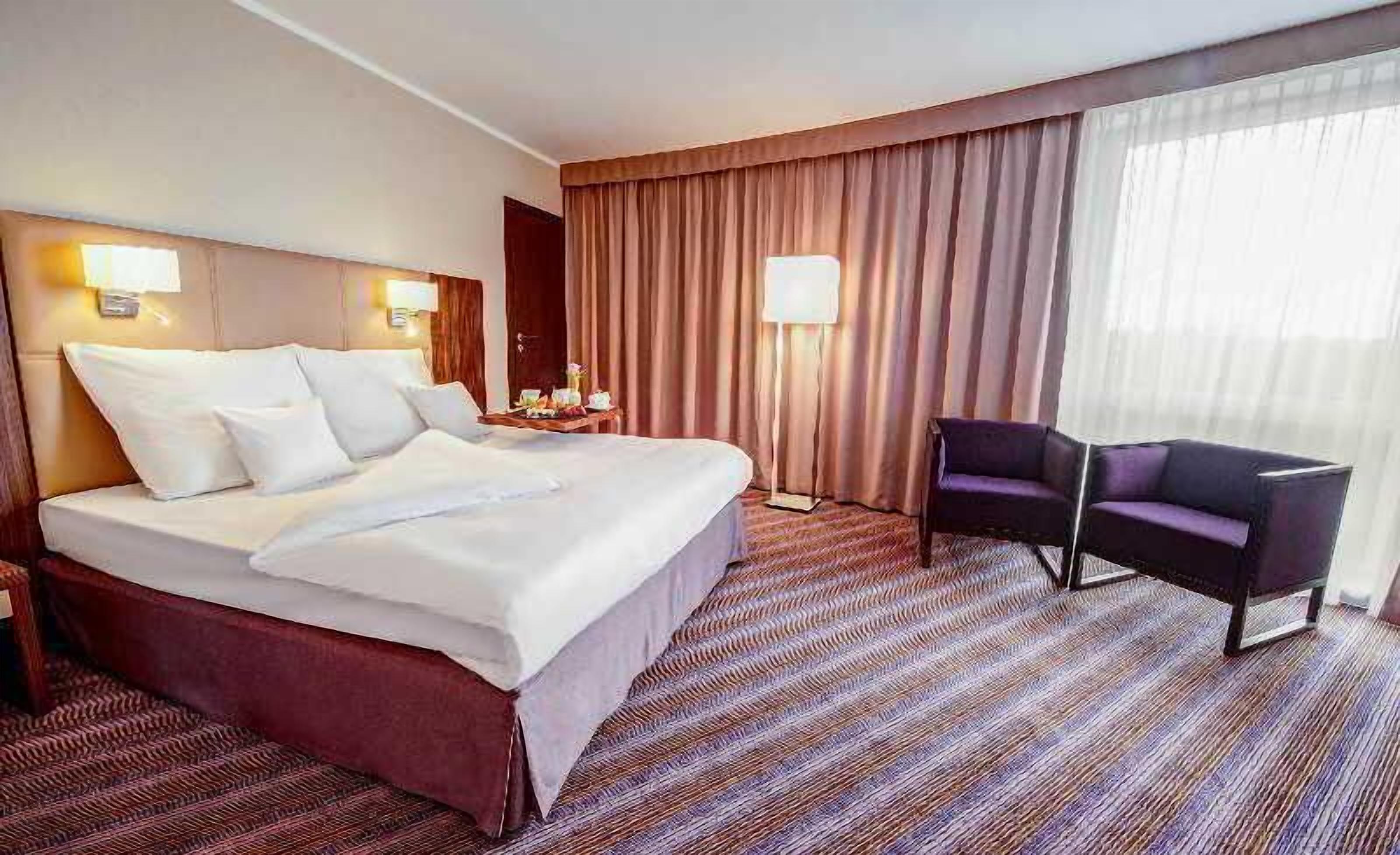 A hotel room with a large bed, a chair, a nightstand, and a lamp.