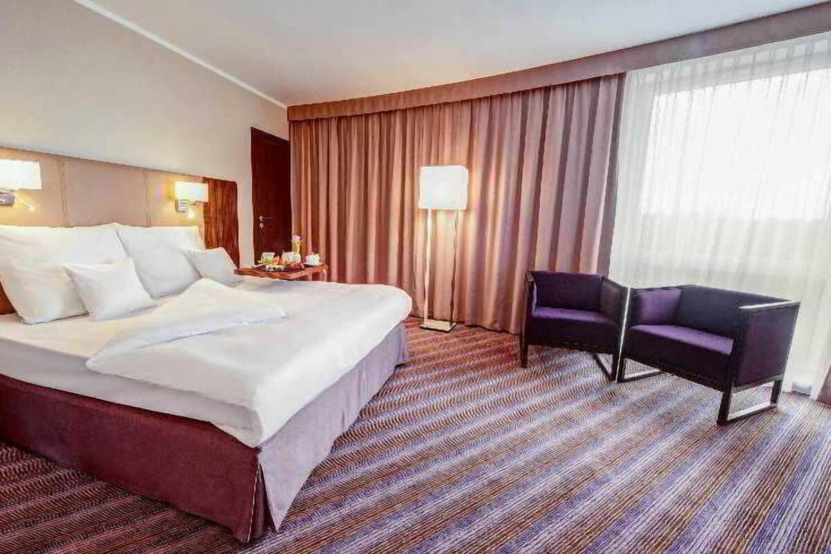 Ein Hotelzimmer mit einem großen Bett, einem Sessel, einem Nachttisch und einer Lampe.