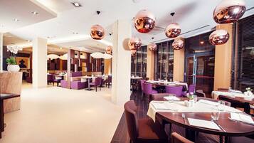 A modern restaurant with round tables, purple chairs, and large spherical light fixtures.