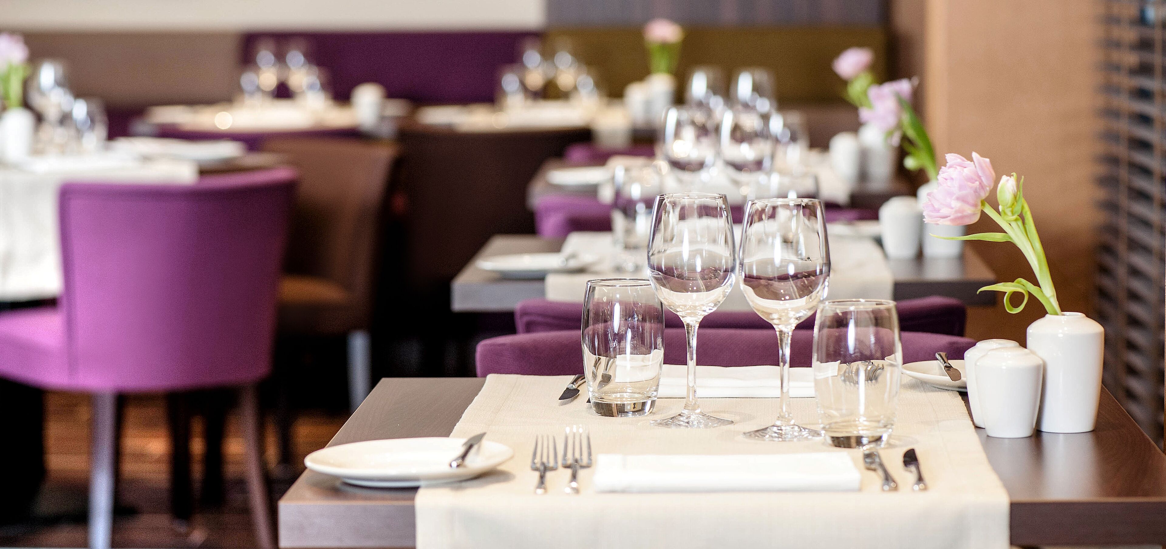 Een restaurant met gedekte tafels, paarse stoelen en witte tafelkleden.