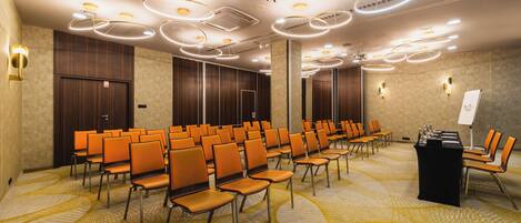Une salle de conférence avec des rangées de chaises orange, un pupitre et un tableau blanc.