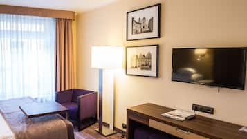A hotel room with a bed, a desk, a chair, a TV, and two framed pictures on the wall.