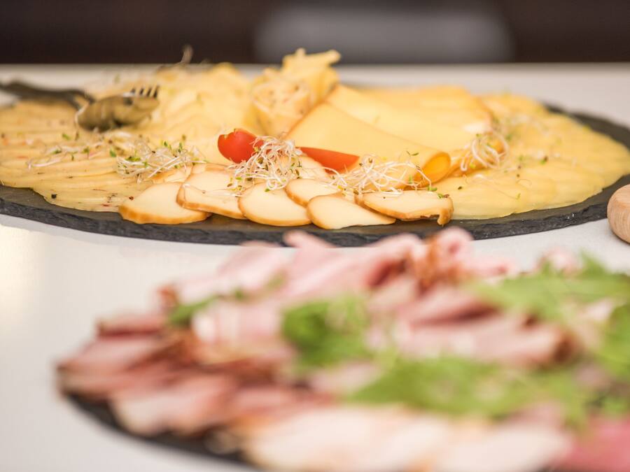 A variety of food items on a slate serving board, including sliced meats, cheese, and garnishes.
