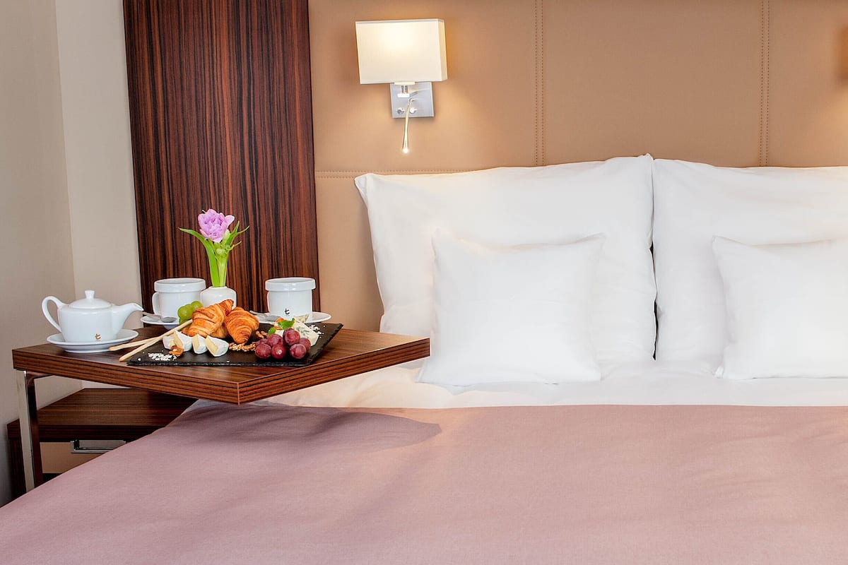 Ein Hotelzimmer mit einem großen Bett, zwei Nachttischlampen, einem Tablett mit Frühstücksangeboten und einem Nachttisch mit Telefon.