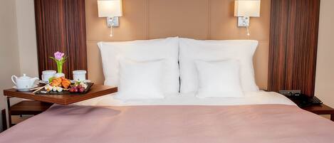Una habitación de hotel con una cama grande, dos lámparas de noche, una bandeja con alimentos para el desayuno y una mesita de noche con un teléfono.