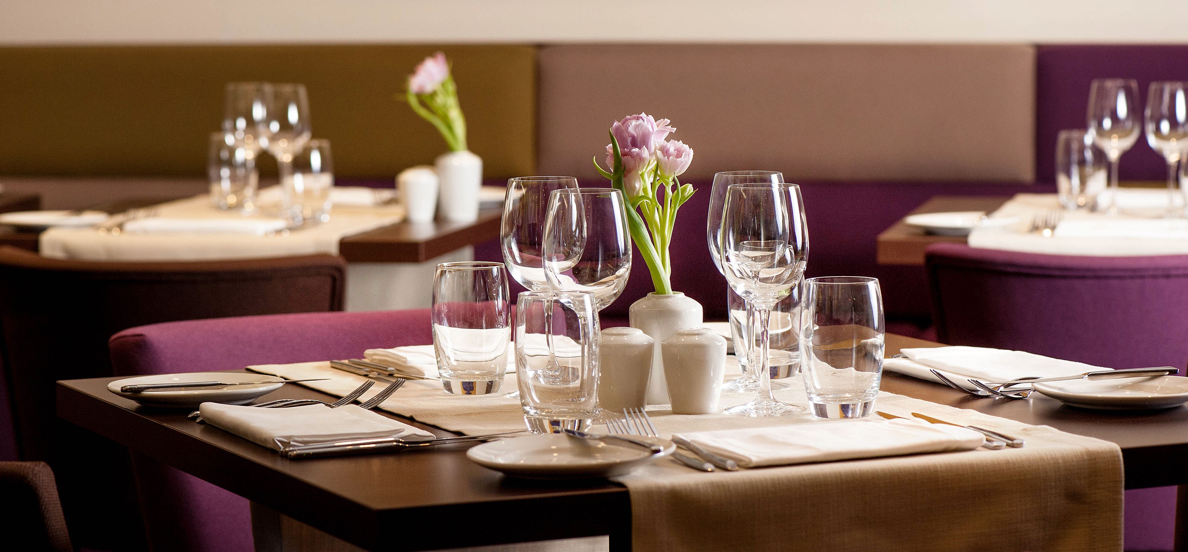 A dining table set with plates, cutlery, glasses, and a vase with flowers.