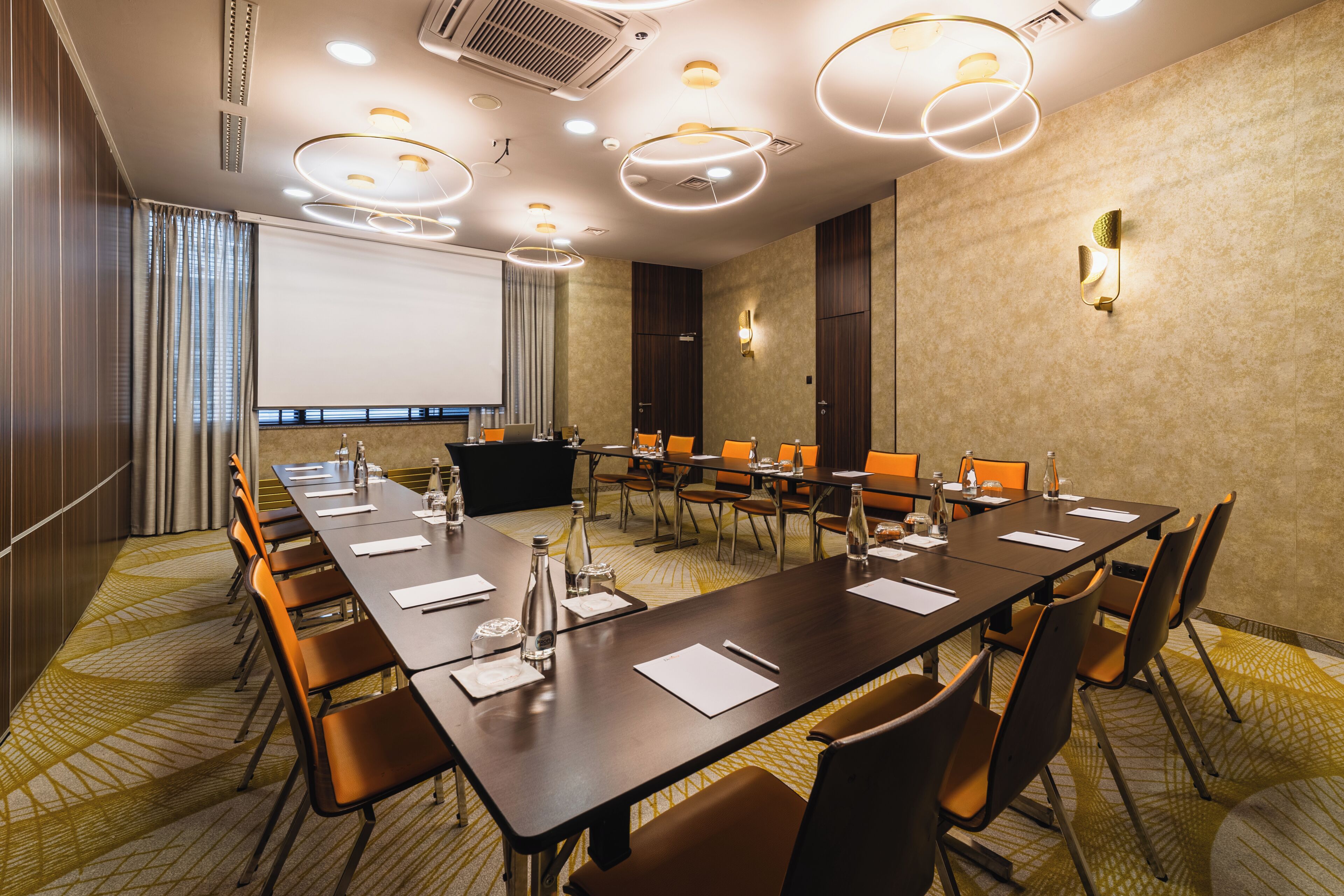 A conference room with a long table, chairs, a projector screen, and a carpeted floor.