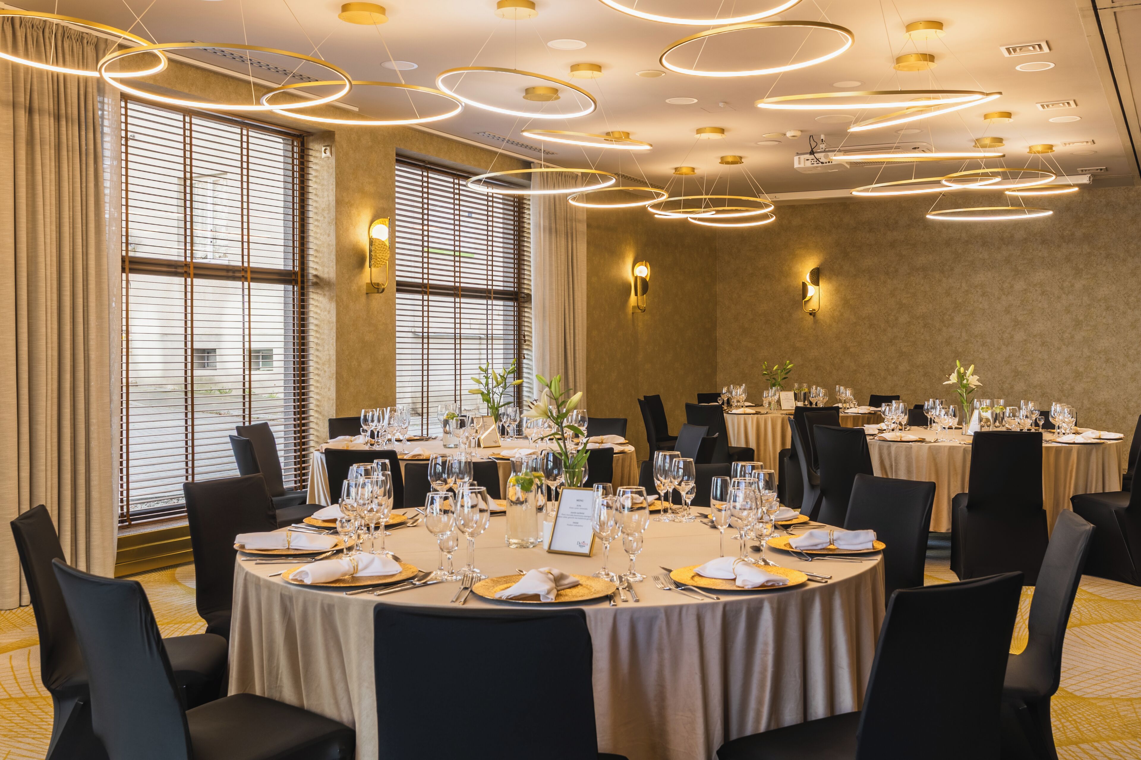 Une salle de banquet avec des tables rondes, des chaises noires et un lustre moderne.