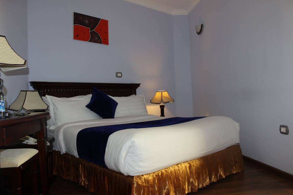 A neatly made bed with white and blue bedding, a wooden headboard, and a bedside table with a lamp.