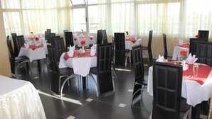 Un espace repas comprenant plusieurs tables, chacune recouverte d’une nappe blanche et agrémentée de serviettes rouges, ainsi que de couverts et de verres.