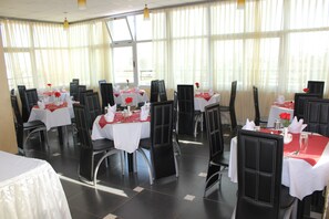 Un comedor con varias mesas, cada una con mantel blanco y servilletas rojas, dispuestas con cubiertos y vasos.