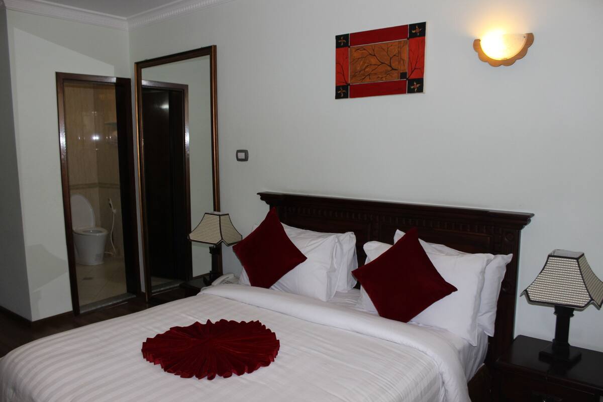 A hotel room with a large bed, a wooden headboard, two bedside lamps, a mirror, and a wall art piece.