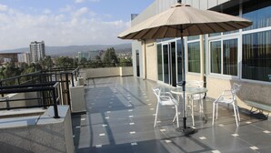 Une terrasse sur le toit, avec une table et des chaises, un grand parasol et une vue sur le paysage urbain.