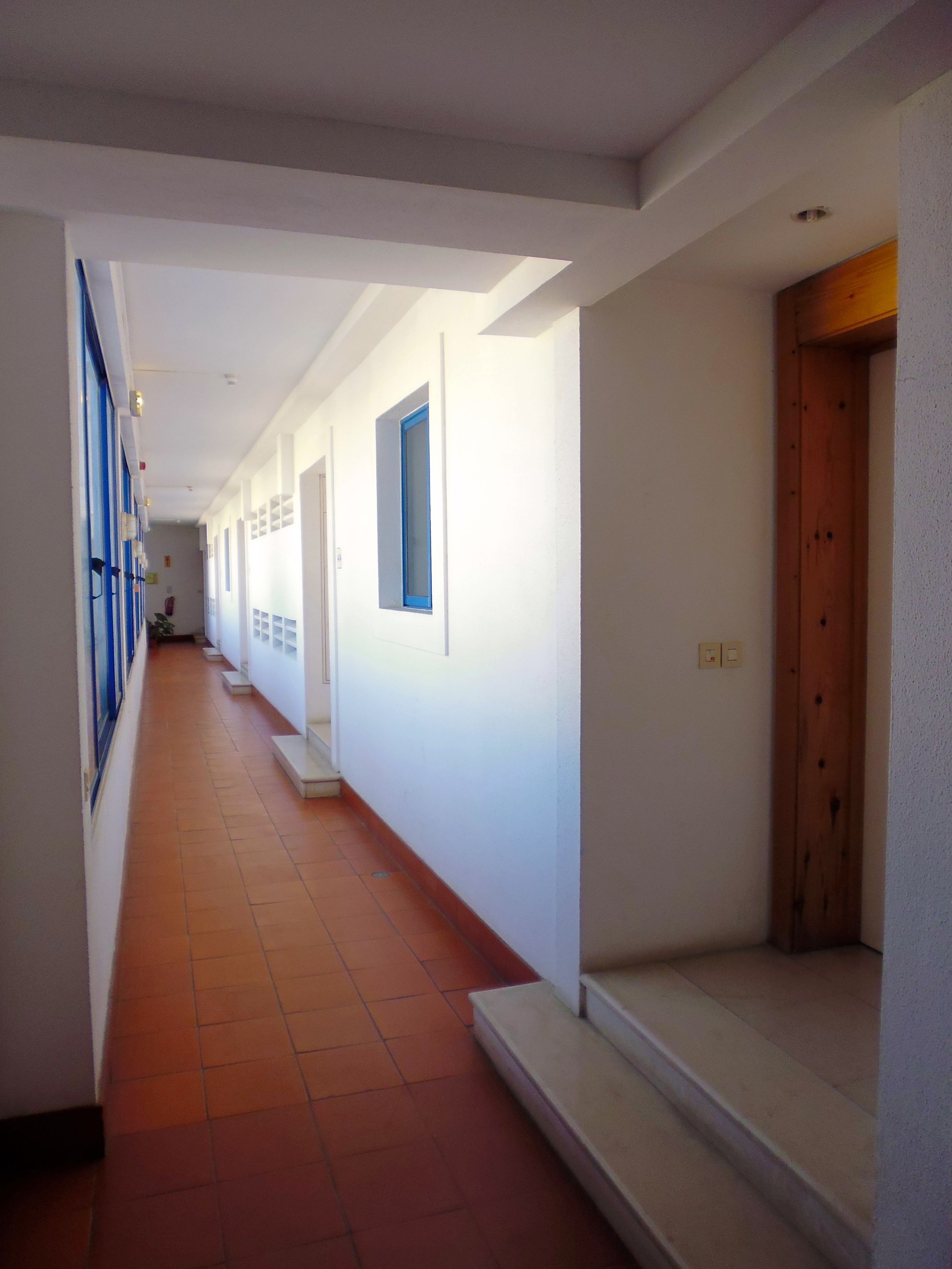 A corridor with white walls, a tiled floor, and a wooden door at the end.