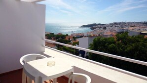 A balcony with a white table and chairs, overlooking a coastal town with buildings and a clear sky. - Almar Hotel Apartamento (Albufeira)